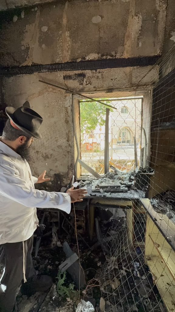 A rabbi gestures at a burnt-out desk and window frame inside the camp building